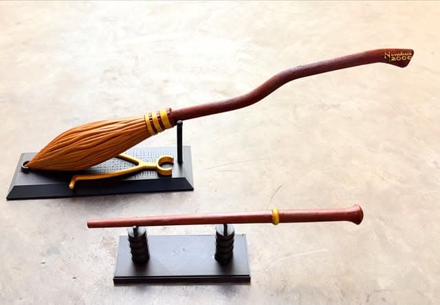 Miniaturas de uma vassoura e uma varinha em suportes pretos